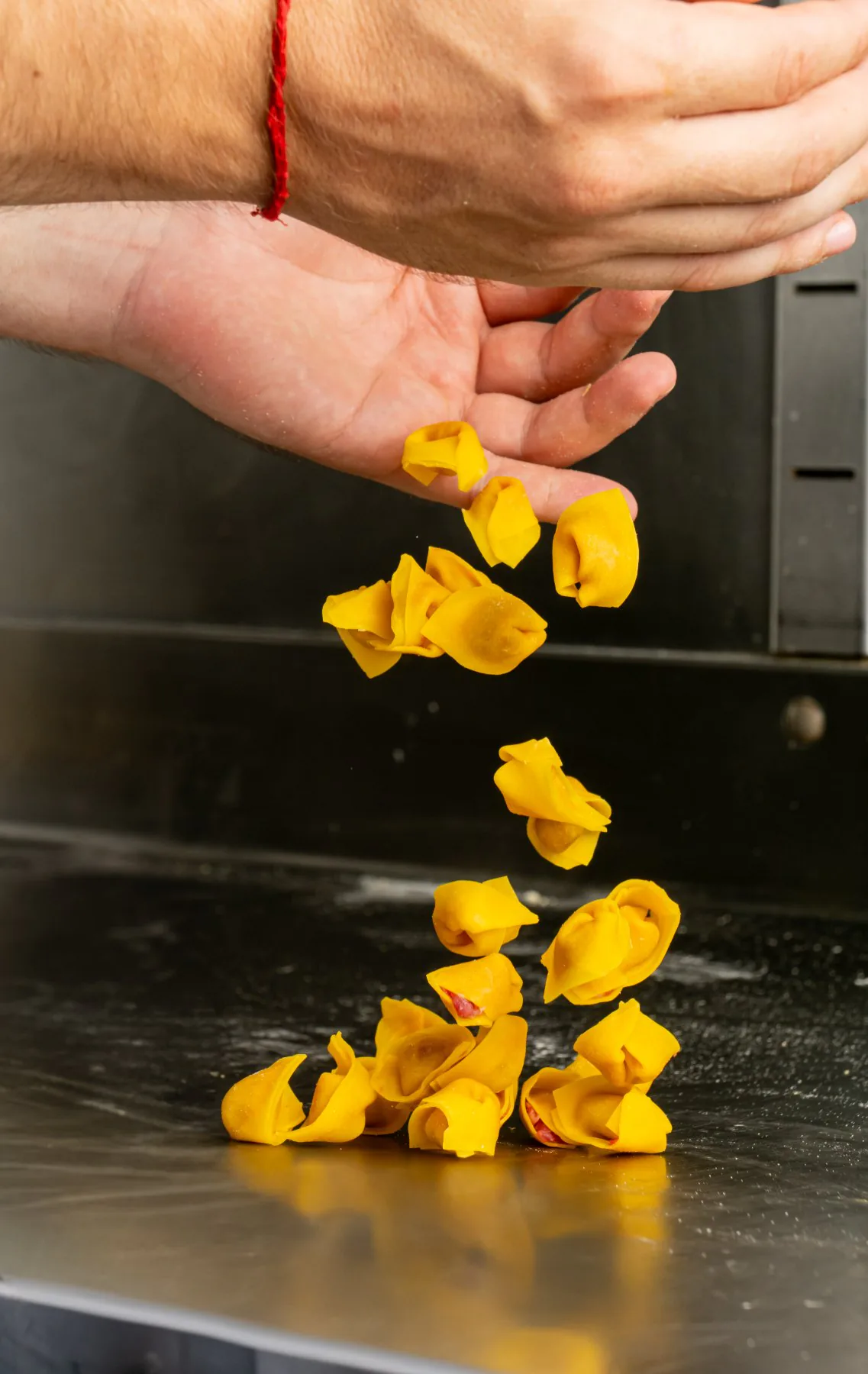 Tortelli appena chiusi che cadono dalle mani sul piano di lavoro